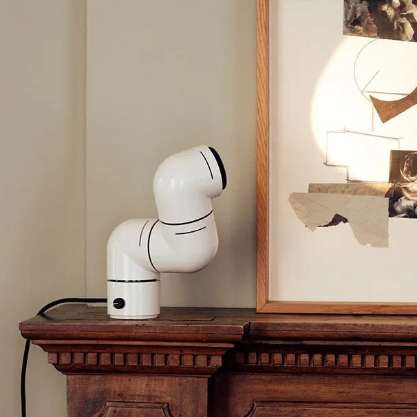 White robot-like device on a wooden surface with a framed picture in the background